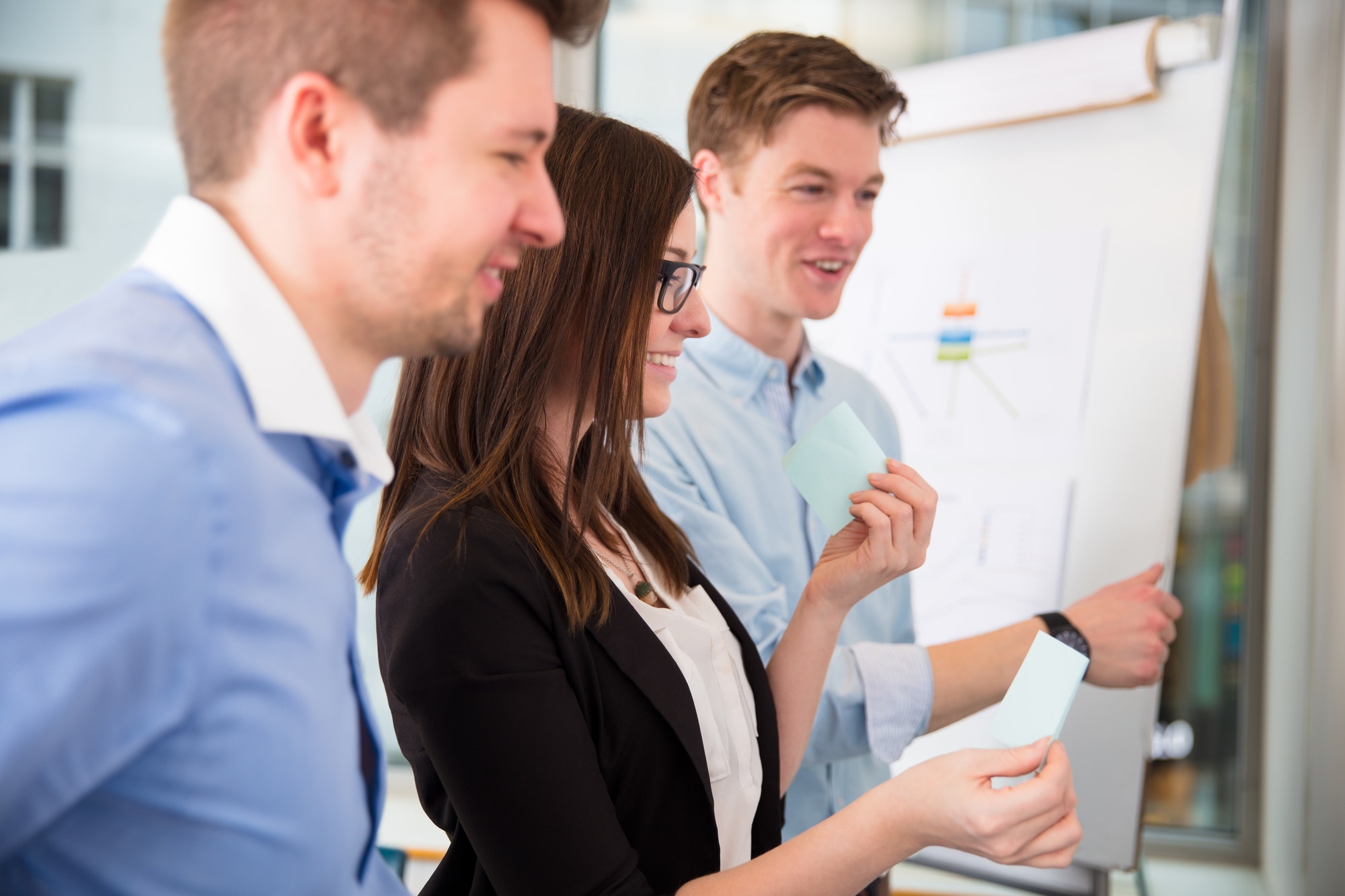 Smiling Businesswoman Holding Adhesive Note By Colleagues